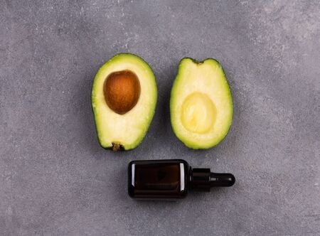 Fresh ripe avocado and avocado oil in little cosmetic bottle on a gray background. Healthy lifestyle concept.の写真素材
