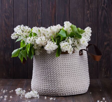 Still life. Bouquet of white lilacs in jute basket on a wooden table. Rustic style. Springtime concept.の写真素材