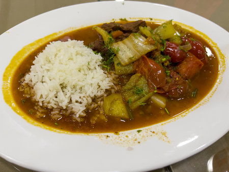 Curry with rice and vegetables on a white plate in a restaurantの写真素材