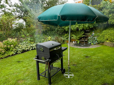 Outdoor barbecue grill with umbrella on green grass in summer garden.の写真素材