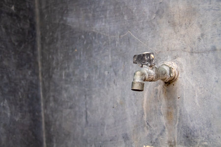 An old water faucet against a gray cement wall in the backgroundの写真素材