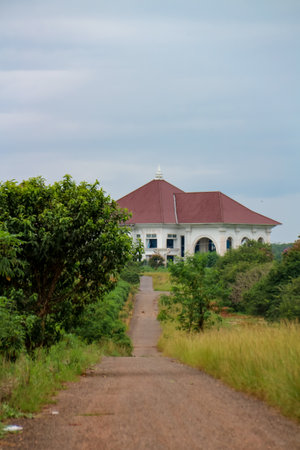 An asphalt road beside a lot of tall grass with a big white house in the backgroundの写真素材