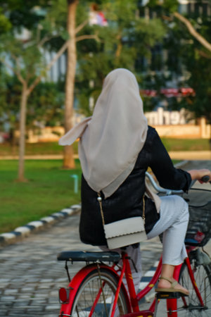 Back view of a muslim woman riding a bicycle in the parkの写真素材