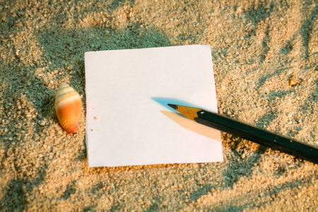 Blank sheet of paper with pencil and seashell on the sandの写真素材