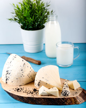 Cheese with black cumin seeds with bottle of milk on wooden background.