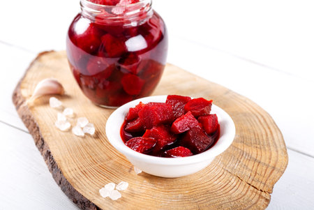 Pickled red betroot in bowl and jar on wooden background.