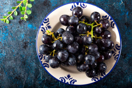 Bunch of grape with water drops in ceramic dish on dark background. Fresh black grapes.の写真素材