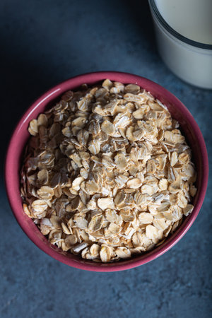 Dry rolled oatmeal in a bowl with milk on dark blue background.の写真素材