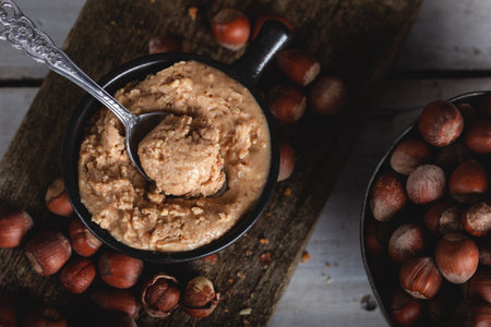 Hazelnut butter in ceramic cup with shelled hazelnuts on wooden background.の写真素材