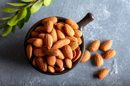Heap of raw almonds in black ceramic bowl on stone background.の写真素材