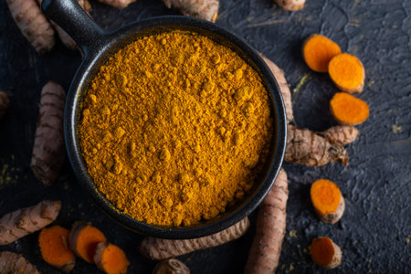 Turmeric powder and fresh turmeric on dark background.