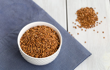 Buckwheat groats in a bowl on a white wooden backgroundの写真素材