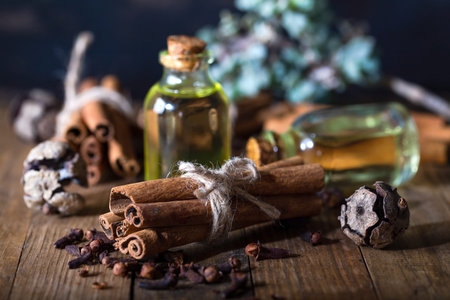 Selection of essential oils with  clove and cinnamon sticks on the wooden background.