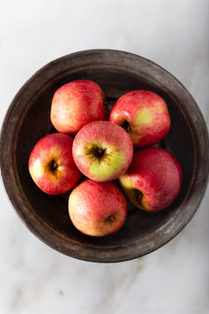 Fresh red apples in rustic plate on white marble background. Top view.