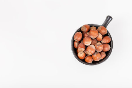 Fresh shelled hazelnuts in a black bowl isolated on white background.の写真素材