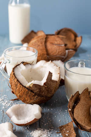 Coconut halves and pieces with glass of coconut milk on a blue natural wooden background.の写真素材