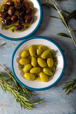Natural black and green olives with rosemary, basil and olive tree leaves on blue wooden background. Top view.の写真素材