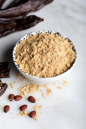 Carob pods and carob powder over a stone background.