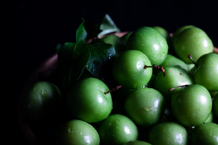 Close-up of fresh green plums in a bowl on dark background. Green plum fruit.の写真素材