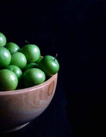 Fresh green plums in a bowl on wooden background. Close-up. Copy space.の写真素材