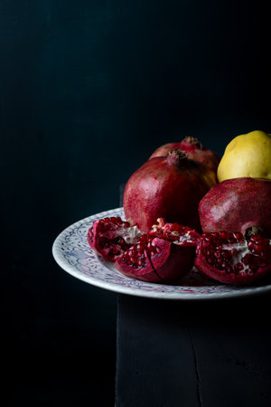 Fresh juicy pomegranate pieces in white porcelain plate on black wooden table. Fresh fruits on dark background.の写真素材