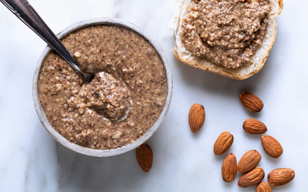 Almond butter in a bowl with almonds on a marble background.