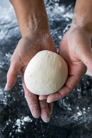 A close-up of a person gently holding a freshly shaped dough ball in their floured hands.