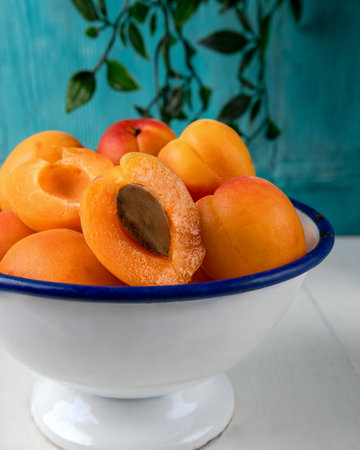 Close-up of fresh ripe apricots in a white enamel bowl with a blue rim, placed on a light background...