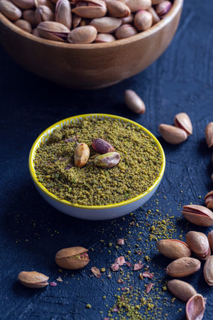 Ground Pistachios and Whole Nuts in Bowl on Dark Background