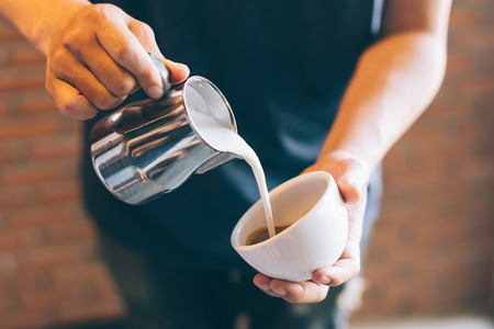 Closeup of male barista holding milk for prepare cup of coffee, latte art.の写真素材