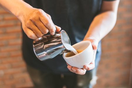 Closeup of male barista holding milk for prepare cup of coffee, latte art.の写真素材