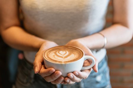 Female hands holding a cup of coffee with foam over wooden table, top view vintage tone.の写真素材