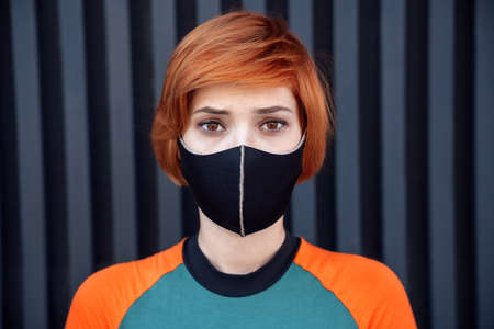 A sad young ginger hipster girl in a dress is standing outside nearby a wallの写真素材