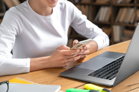 Close-up photo of female student hands using mobile phone for studying at home.