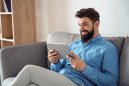 Smiling millennial caucasian man watching funny video using mobile tablet