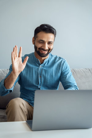 Portrait of indian business man waving hand to online interlocutor using laptop