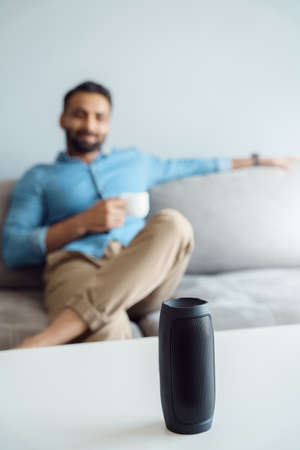 Focus on wireless speaker assistant and relaxed indian man with cup of coffeeの写真素材