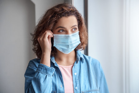 Close-up portrait of young woman wears protective mask indoor.