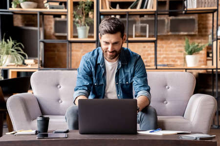 Handsome smiling caucasian man freelancer using laptop at home in living roomの写真素材