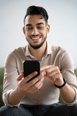 Happy young man laughing looking at cell phone sitting in living room at homeの写真素材
