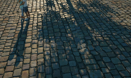 Romantic teen couple hugging on cobblestone road at reddish sunset Sun down creates a beautiful long shadow of the couple and huge shadow of a tree on cobblestones.   Wide angle waist down shot.の写真素材