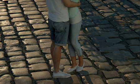 Romantic teen couple hugging on cobblestone road at reddish sunset.  Under waist shot.の写真素材