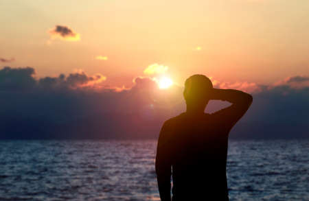 Back view silhouette photo of depressed man watching the sunset on the sea. Thoughtful, overthink, pensive and future plans concept.の写真素材