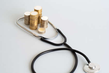 Close up photo of stethoscope and stacked coins on isolated background. Concept of rising costs of healthcare expenses.の素材 [FY310190070292]