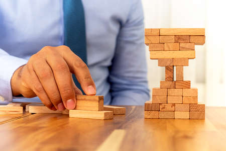 Man building wooden blocks shape of hour glass. Business and time management concept.の写真素材