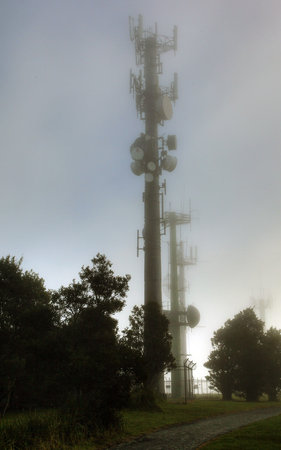 communication towers shrouded in mist against greenの写真素材