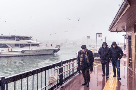 Unidentified man walking near Karakoy Uskudar pier on a snowy day in winter.New mosque is on the background.Istanbul,Turkey,07 January 2017のeditorial素材