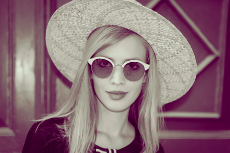 Young attractive woman in fashionable black dress,and stylish round sunglasses and yellow hat poses in front of wall  at street.Retro and vintage filter and colors effect used.
の写真素材
