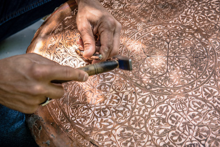 Senior craftsman,tinsmith,working with hammer during hand stamping or engraving decoration pattern on metal plate.Copper master, hands detail of craftsman at work.の写真素材