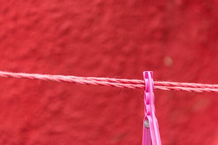 Vintage view of pink Clothes peg pinned to a bench with red wall in a background hanging on a clothes rack
の写真素材